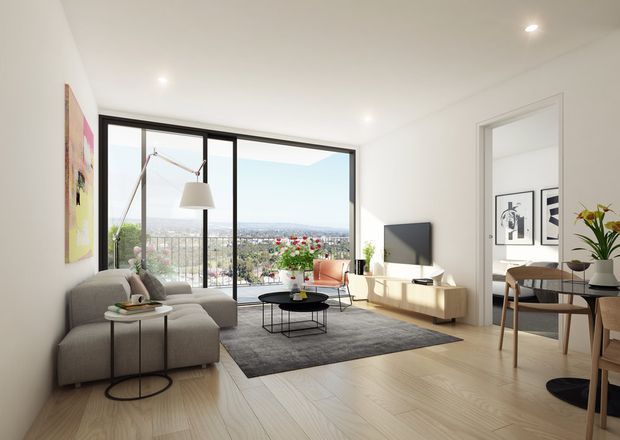 Bright, contemporary open-plan living room with pale timber flooring, white walls and ceiling, a large black-framed glazed opening overlooking a distant urban landscape, and restrained modern furnishings. The room includes a grey sectional sofa, round coffee tables, a dark area rug, sculptural floor lamp, wall-mounted television with low timber joinery, and an adjacent dining area visible through a wide opening.
