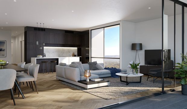 Open-plan contemporary living, dining, and kitchen interior with floor-to-ceiling glazing and expansive views. The room features a dark timber kitchen with a pale stone island, light upholstered seating, a patterned rug, herringbone timber flooring, black-framed glazing, and restrained modern furnishings. A dining area occupies the foreground, with the lounge and kitchen arranged beyond.