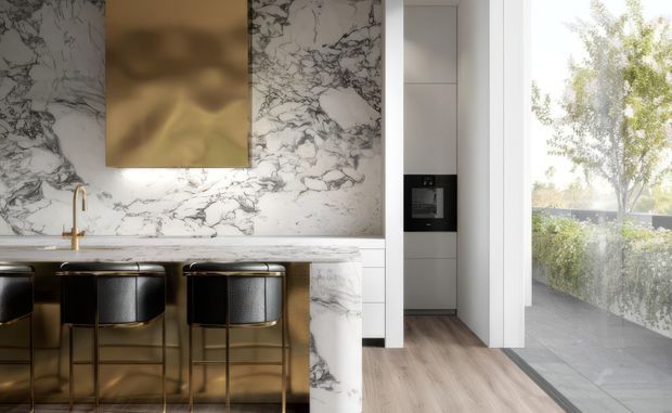 Luxurious contemporary kitchen with a dramatic white-and-grey veined marble backsplash and waterfall island. The island features a warm metallic base and three dark upholstered bar stools with brass-toned frames. Integrated cabinetry and appliances sit to the right, while full-height glazing opens to a planted outdoor terrace. The space has warm, refined finishes and abundant natural light.
