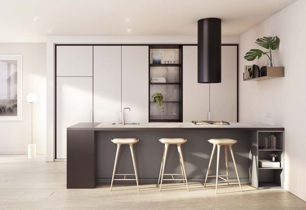 A bright, contemporary open-plan kitchen with a dark island featuring seating for three, white full-height cabinetry, an integrated open display niche, a pale benchtop, brass-toned tapware, and a large black cylindrical rangehood. Light timber flooring and minimal shelving with indoor plants complete the clean, refined interior.