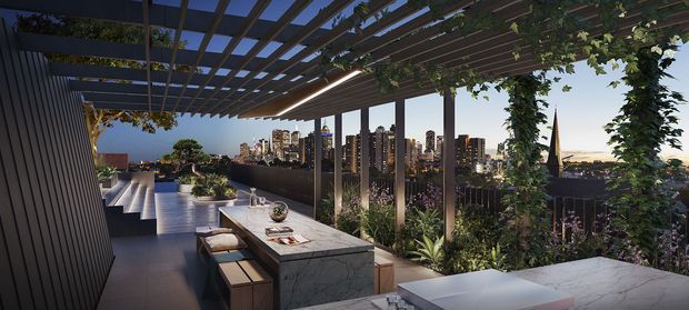 A sophisticated rooftop terrace at dusk with a covered timber pergola, climbing greenery, built-in outdoor kitchen or bar island, dining and lounge furnishings, and a dramatic urban skyline beyond. The space uses dark decking, stone surfaces, vertical screening, integrated planting, and warm architectural lighting to create a refined outdoor entertaining area.