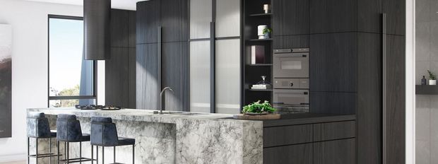 Contemporary kitchen featuring a large pale stone island with waterfall edge, dark vertically textured cabinetry, integrated stainless-steel appliances, open shelving, and a row of upholstered bar stools. Tall glazing and a minimalist black-framed partition bring natural light into the space.