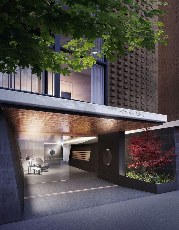 A contemporary apartment or hotel entrance beneath a projecting concrete canopy. The entry features dark metal framing, large glazed openings, a textured metallic soffit, dark tiled or stone walls, patterned brick breeze-block detailing, and a sheltered lobby with seating. Integrated planter beds with a red ornamental tree soften the urban facade, while mature foliage frames the upper level.