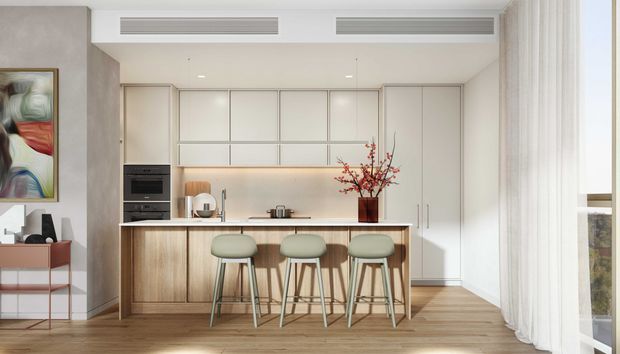 Bright contemporary open-plan kitchen with a large light timber island, three green upholstered bar stools, integrated pale cabinetry, built-in appliances, and a neutral stone-toned benchtop. Floor-to-ceiling sheer curtains and a large window bring in abundant natural light, while an abstract artwork and sculptural vase add restrained colour.