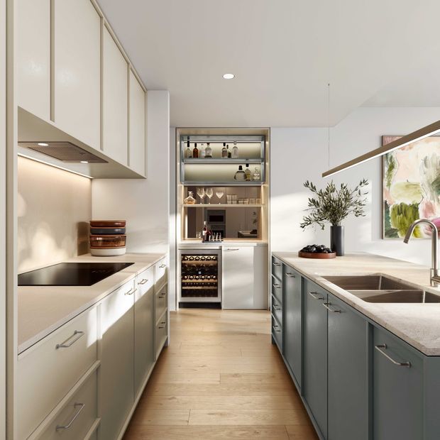 A refined contemporary kitchen with a galley-style layout and a central island. The room features pale wood flooring, warm white upper and lower cabinetry on one side, dark grey-green island cabinetry, integrated appliances, a pale stone benchtop, under-cabinet lighting, and a built-in drinks and wine storage display at the rear. A stainless-steel sink and brushed metal tap sit beneath a large botanical artwork, with restrained decorative styling including olive branches and ceramics.