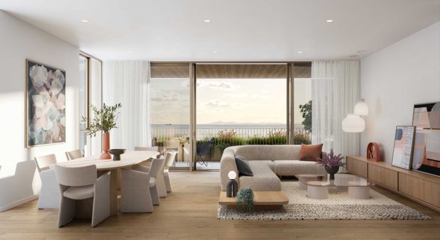 A bright, open-plan contemporary living and dining area with pale timber flooring, white walls, and expansive floor-to-ceiling glazed doors opening to a balcony with a distant coastal or waterfront outlook. The dining area has a light timber table and upholstered chairs, while the living area features a curved neutral sectional sofa, timber media cabinetry, layered rugs, sculptural pendant lighting, and restrained artwork and planting.