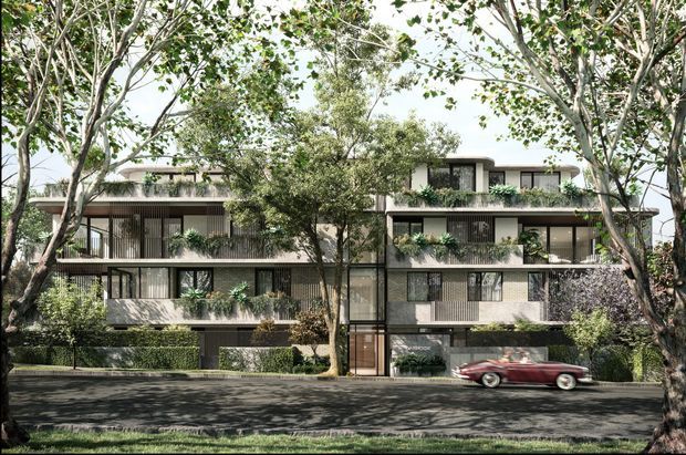 A landscaped streetscape view of a contemporary multi-storey apartment building framed by mature trees. The facade combines light rendered walls, extensive glazing, dark metal window and balcony frames, recessed balconies, vertical screening and planted balcony greenery. A central glazed entry is visible at ground level, with hedges and garden planting along the frontage.