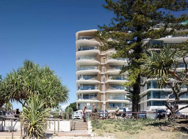 Exterior view of a contemporary multi-storey apartment building with rounded stacked balconies, extensive curved glazing, and light-coloured facade elements. Coastal vegetation, sandy landscaping, and a bright blue sky surround the building, with people and cars visible at ground level.