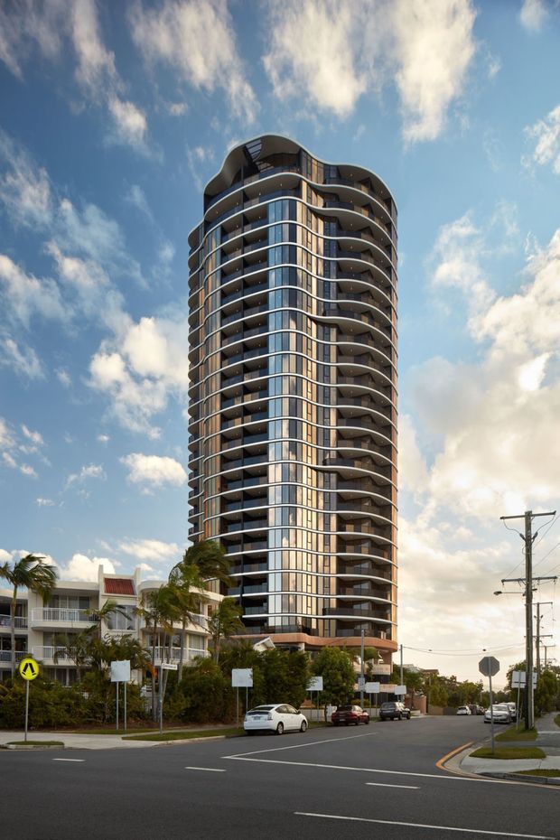 Street-level exterior view of a tall contemporary residential apartment tower with rounded corners, extensive glazed curtain walling, stacked balconies, and organically curved floor plates. The tower rises above a lower-rise streetscape with palm trees, roads, utility poles, and neighbouring buildings under a partly cloudy sky.