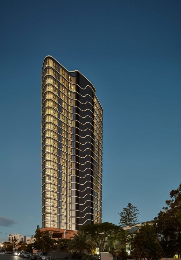 A dusk exterior photograph of a tall, slender multi-storey residential tower. The building has extensive floor-to-ceiling glazing, rounded corners, curved balcony edges and repeated undulating horizontal bands, with warm interior lighting visible through the windows. Landscaping and low-rise buildings surround the base, while the dark blue evening sky forms the background.