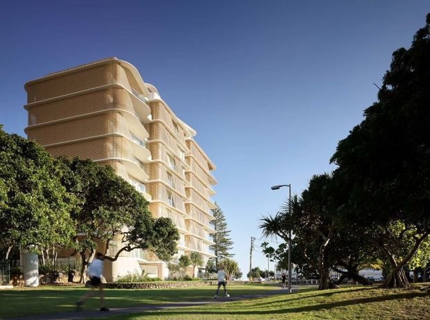 Exterior architectural view of a multi-storey apartment building with rounded, projecting balconies and light cream facade detailing, set beside a landscaped public or communal green space with mature trees. The image is photographed from ground level under clear skies.