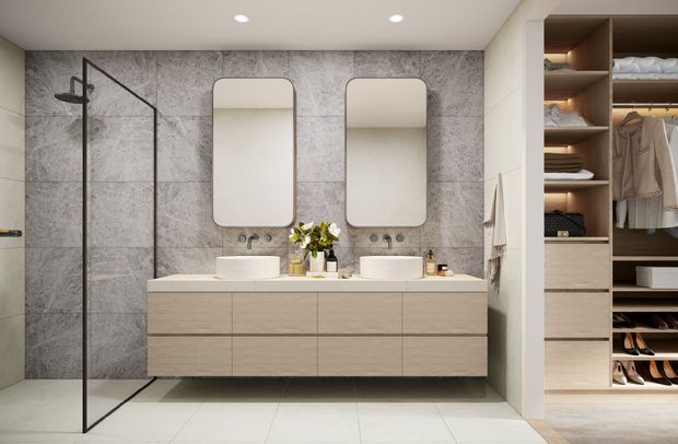 Contemporary bathroom with a double vanity, two rounded-rectangle mirrors, wall-mounted light wood cabinetry, grey stone-look wall tiles, a frameless black metal shower screen, and pale floor tiles. An open walk-in wardrobe is visible through the opening on the right.