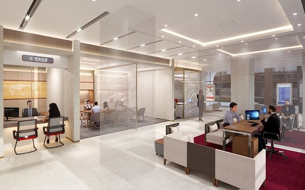 A bright contemporary commercial interior, likely a hotel or office reception and lounge area. The open-plan space features a reception desk with seating, glass-partitioned meeting or work areas, lounge seating around wood tables, desks with computers, pale stone-look flooring, illuminated wall panels, and a layered recessed ceiling with linear lighting. People are using the reception, meeting, and work areas.