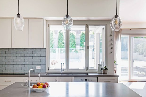 Bright, contemporary kitchen with white shaker-style cabinetry, a grey subway-tile splashback, a large island with sink and pendant lights, and generous glazing overlooking an outdoor area.