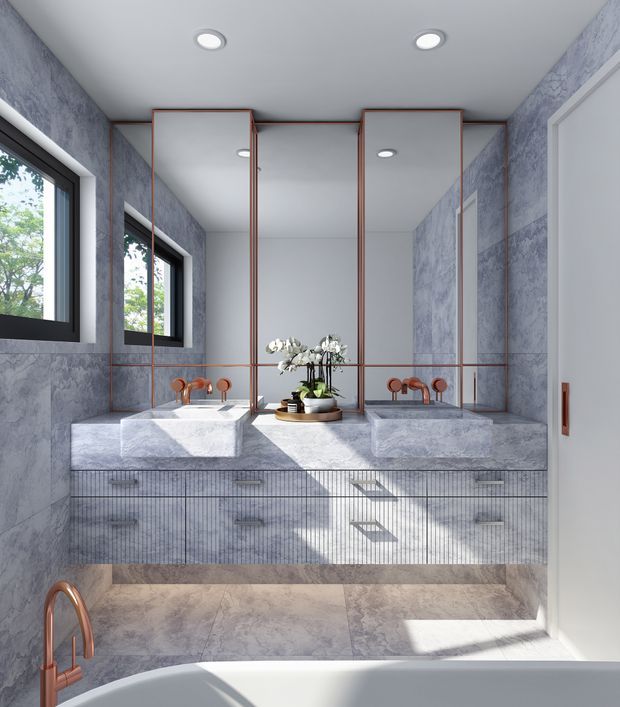 A bright, refined bathroom featuring a double vanity with two white stone vessel basins, extensive grey marble-effect wall and floor finishes, vertically fluted vanity cabinetry, large mirrored panels with slim warm metal edging, and black-framed windows. A freestanding bathtub is partially visible in the foreground, with copper-toned tapware and soft natural light.