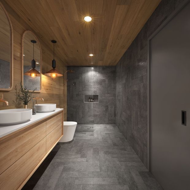 Contemporary bathroom with a long floating timber vanity, two white vessel basins, arched timber-framed mirrors, wall-mounted pendant lights, a wall-hung toilet, and a walk-in shower at the rear. Large-format grey stone-look tiles cover the floor and shower walls, while the ceiling and vanity use warm timber finishes.