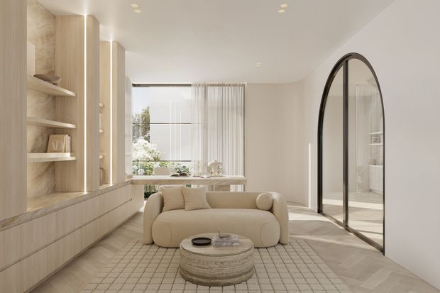 A softly lit, refined contemporary living room with warm light-wood built-in cabinetry and open shelving along one wall, a sculptural cream boucle sofa, round textured coffee table, and a large pale grid-patterned rug. Floor-to-ceiling glazing with sheer curtains brings in greenery and daylight, while a dramatic black-framed arched glass doorway leads to an adjacent space. The room has a calm, neutral palette and curved, minimalist forms.