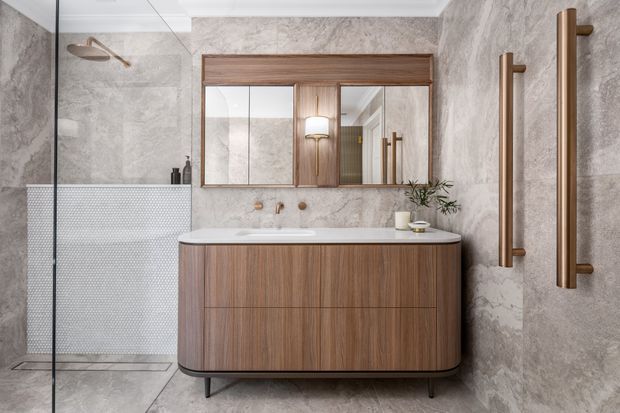 A refined contemporary bathroom featuring a floating timber vanity with integrated basin, large mirrored cabinet, grey marble-look wall and floor surfaces, a glass-enclosed shower, and brushed brass fixtures and heated towel rails.