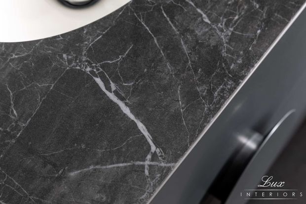 Close-up detail of a dark charcoal-black marble surface with prominent white veining, adjacent to dark cabinetry or joinery with a curved metallic handle. A partial white circular basin or fixture is visible at the upper left, suggesting a refined bathroom or vanity setting.
