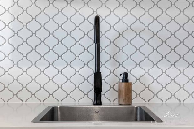 Close-up of a kitchen sink with a deep stainless-steel undermount basin, dark gooseneck tap, and wood-toned soap dispenser. The backsplash is covered in a repeating quatrefoil-patterned tile, creating a refined contemporary feature behind the sink.