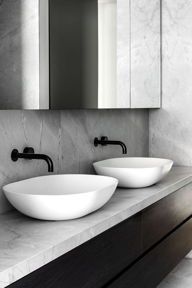 A contemporary double-vanity bathroom featuring two white vessel basins on a grey marble-look stone benchtop, with matching grey wall cladding, matte black wall-mounted taps, dark timber-look vanity cabinetry, and mirrored wall cabinets.