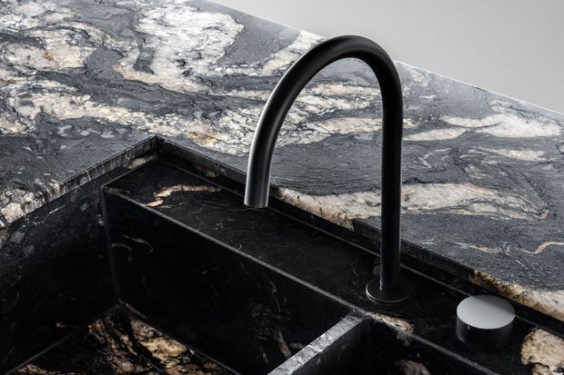 Close-up of a contemporary kitchen sink area featuring a matte black curved gooseneck tap, integrated black sink, and dramatic dark veined stone benchtop and splashback.