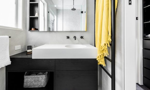 Contemporary bathroom with a wall-mounted white basin and integrated benchtop above dark timber cabinetry, matte black tapware, a large mirrored cabinet, and a glass-enclosed shower. A bright yellow towel adds a bold accent against the neutral grey and black finishes.