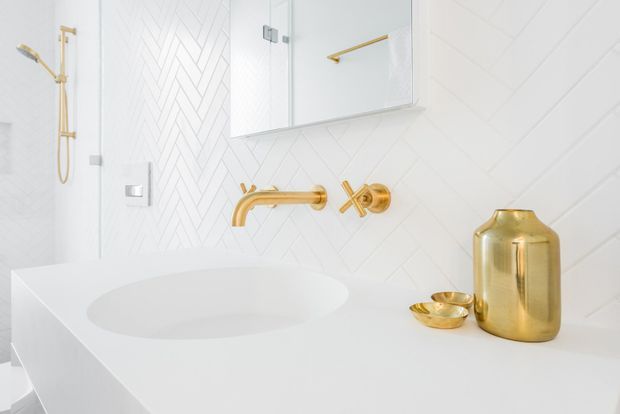 Bright, refined contemporary bathroom featuring a white floating vanity with integrated basin, white geometric and herringbone wall tiles, frameless glass shower enclosure, mirrored cabinet, and polished gold wall-mounted tapware and accessories.