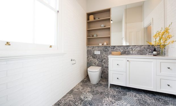 Bright contemporary bathroom featuring white subway-tile walls, a patterned monochrome floor and matching splashback, a wall-mounted white vanity with integrated storage, mirrored cabinet doors, open timber shelving, and a white toilet. Natural light enters through the large window.