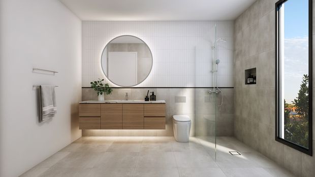 Contemporary bathroom with a floating timber-veneer vanity, round wall mirror, wall-mounted basin, toilet, and open glass shower. Large-format pale stone-look floor tiles and grey concrete-look wall tiles create a restrained neutral palette, while a narrow vertical white tile feature wall adds texture. A tall window brings in natural light and views of greenery.