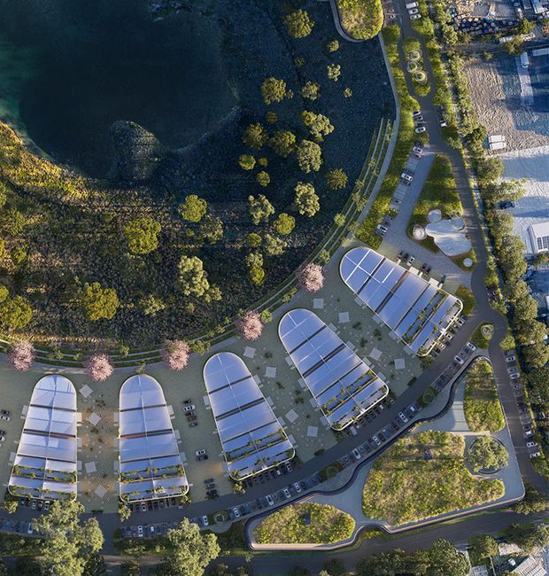 Aerial architectural masterplan view of a landscaped development beside a large body of water. Several elongated, rounded-roof glazed buildings are arranged along curving internal roads and planted pedestrian areas, with parking, gardens, and extensive mature tree cover.