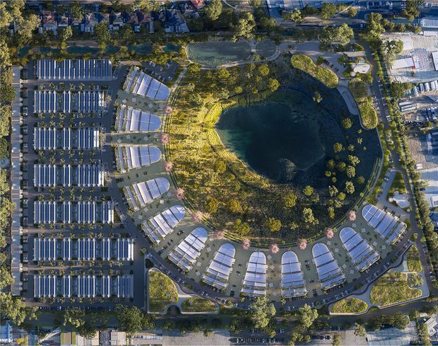 Aerial masterplan view of a large landscaped site organised around a central oval pond or lake. Repeated curved-roof buildings and extensive parallel-roof structures form a circular and grid-like development, connected by landscaped paths, roads, and planted areas. The image reads as a planned commercial or institutional campus rather than an individual interior space.