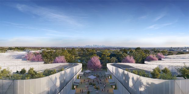 Aerial architectural rendering of a large contemporary development with two sweeping white pavilion-like buildings framing a landscaped central pedestrian plaza. The buildings feature curved forms, translucent or light cladding, planted rooftop terraces, and mature trees with pink flowering canopies. A dense urban skyline is visible in the distance beneath a bright blue sky.