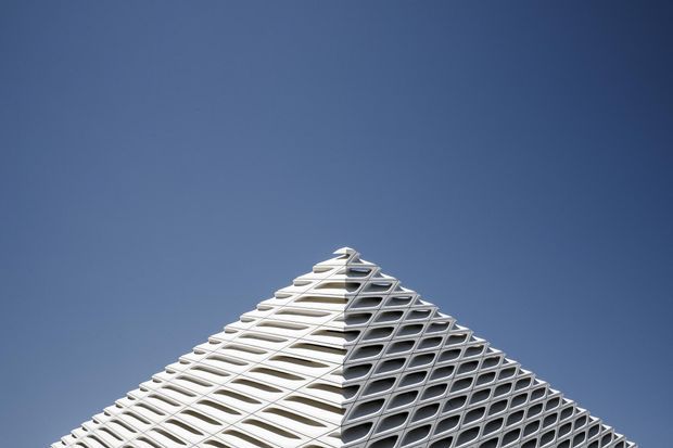 Close-up architectural view of the pointed upper corner of a modern high-rise building, featuring a distinctive geometric grid facade with repeating rounded rectangular openings against a clear blue sky.