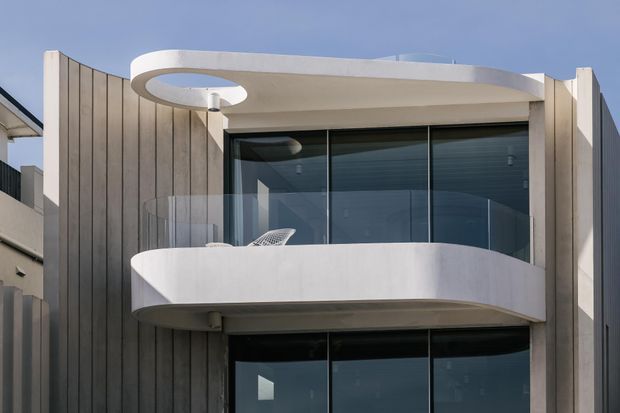 Contemporary multi-storey residential facade with vertically ribbed dark cladding, expansive dark glazing, and distinctive curved white balconies. A sculptural oval roof opening and rounded balcony forms create a strong modern architectural expression.