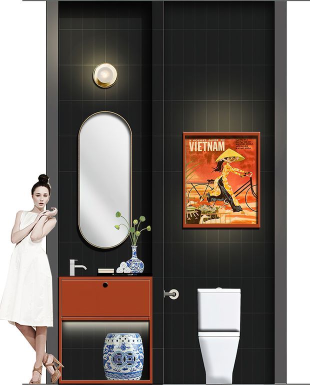 A compact, dramatically styled bathroom with charcoal-black tiled walls, a wall-mounted terracotta-red vanity, white basin and chrome tapware, an arched pill-shaped mirror with a slim metallic frame, and a white modern toilet. Decorative blue-and-white ceramics, a small vase of greenery, a round wall light, and a framed vintage Vietnam poster add character. The high-contrast scheme and sculptural fixtures create a refined, eclectic, slightly art-deco-inspired interior.