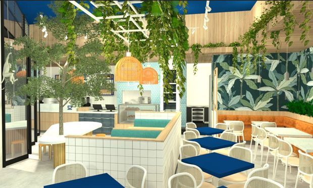 Bright contemporary commercial hospitality interior, likely a café or restaurant, with a tiled service counter and integrated display case, numerous blue-topped tables, white chairs, indoor trees and hanging greenery, timber wall cladding, botanical wallpaper, and a blue ceiling. The space has a lively indoor-garden character with strong graphic and natural accents.