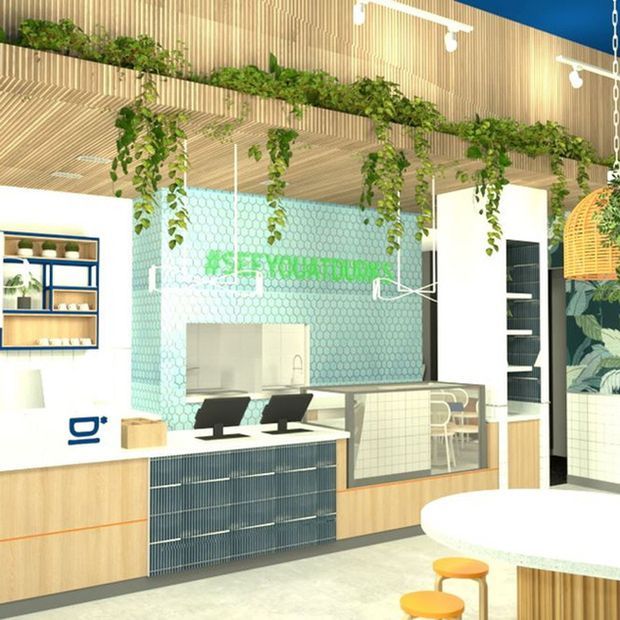 Bright contemporary commercial interior with a reception or service counter, integrated shelving and cabinetry, pale timber slatted ceiling, hanging greenery, and a turquoise hexagonal-tile feature wall. The space includes a small seating area, glazed partitioning, and decorative pendant lighting, creating a fresh biophilic workplace or hospitality setting.