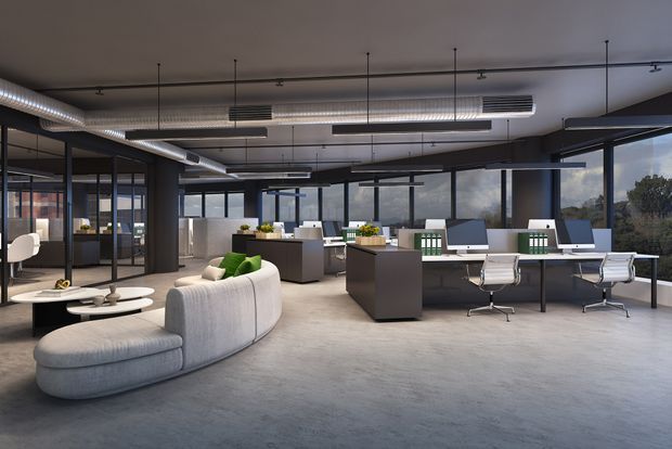 A spacious contemporary open-plan office interior with exposed ductwork, suspended linear lighting, dark-framed floor-to-ceiling glazing, individual workstations, meeting desks, and a curved light-grey lounge sofa. The space has polished concrete flooring, dark structural framing, and views of greenery outside.