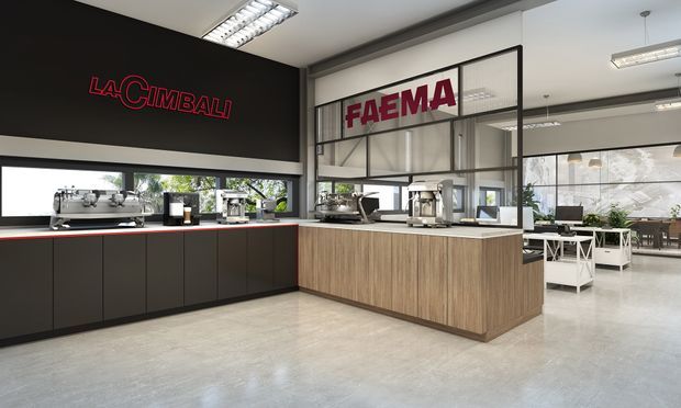 A modern commercial coffee showroom or café training space with espresso machines displayed along a long black counter and a central timber-clad service island. Large black-framed glazed partitions, exposed-style ceiling services, polished concrete flooring, and prominent La Cimbali and Faema signage define the industrial-inspired fit-out.