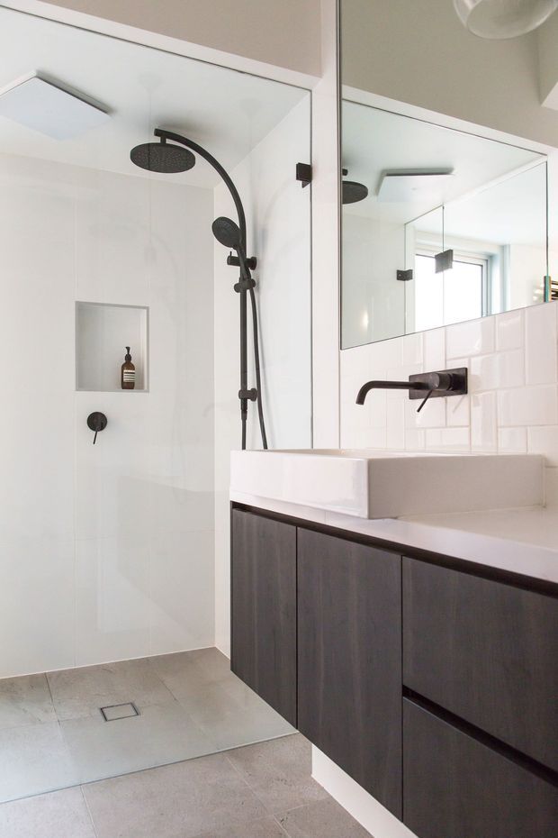 Contemporary bathroom featuring a frameless glass shower enclosure with matte black rainfall and handheld shower fittings, a recessed wall niche, large wall mirror, white rectangular vessel basin, dark wood vanity cabinetry, white tiled splashback, and light grey floor tiles.