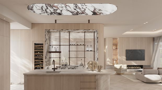 A warm, refined open-plan interior viewed from the kitchen. A large light-wood island with a pale stone benchtop occupies the foreground, with a sculptural marble-patterned ceiling feature above. Behind the island is a framed glass and dark metal display partition, wine storage, and integrated shelving. The living area beyond includes a wall-mounted television, linear fireplace, cream seating, and sheer curtains. The space is softly lit with a neutral beige, cream, light-wood, and dark accent palette.