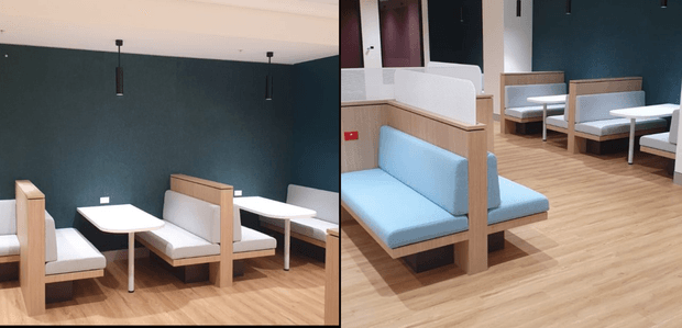 Bright contemporary commercial seating area with multiple built-in booth-style benches, pale blue upholstered cushions, light timber partition frames, white tabletops, and a dark teal feature wall. The space has light timber flooring, simple pendant lights, and a clean hospitality or waiting-area layout.