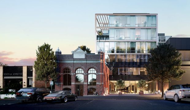 Street-facing architectural rendering of a contemporary multi-storey development combining a restored red-brick heritage facade with a tall glazed apartment or commercial building behind and above it. The frontage includes large arched windows, extensive floor-to-ceiling glazing, balconies, and a ground-level retail or lobby frontage. Adjacent low-rise commercial buildings, street trees, bicycles, and parked cars are visible.
