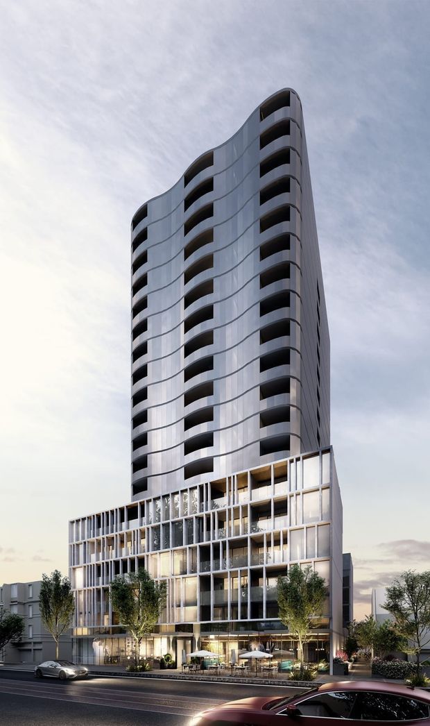 Architectural rendering of a tall contemporary apartment or mixed-use building viewed from street level. The tower has a rounded, sculptural form with repeated recessed balconies and a pale metallic or concrete façade, rising above a lower multi-storey podium with extensive vertical glazing and expressed framing. Street-level retail or hospitality spaces, outdoor seating, landscaping, and surrounding urban buildings are visible.