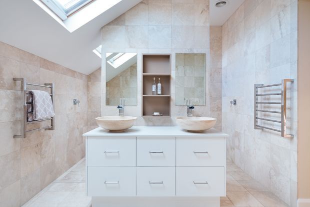 Bright, spacious contemporary bathroom with a symmetrical double vanity, two vessel basins, wall-mounted mirrors, open shelving, heated towel rails, and full-height pale stone-look tiling. A large skylight brings in abundant natural light, while white cabinetry and chrome fixtures create a clean, refined finish.