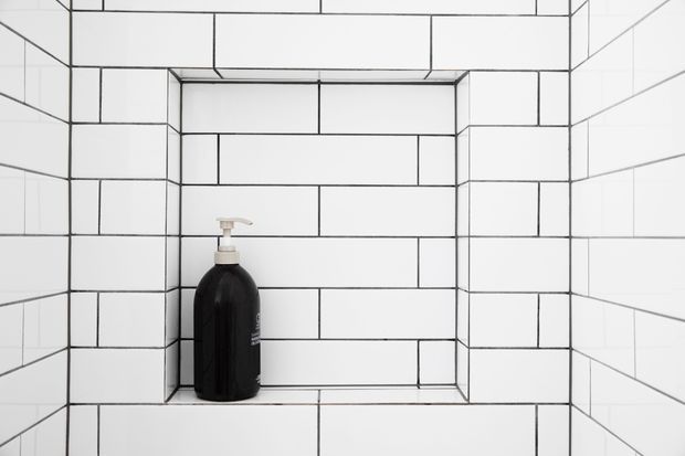 Close-up of a recessed wall niche lined with white rectangular subway tiles and contrasting dark grout. A single black pump bottle sits on the tiled niche shelf. The image focuses on the tiled architectural detail, with no broader room context visible.