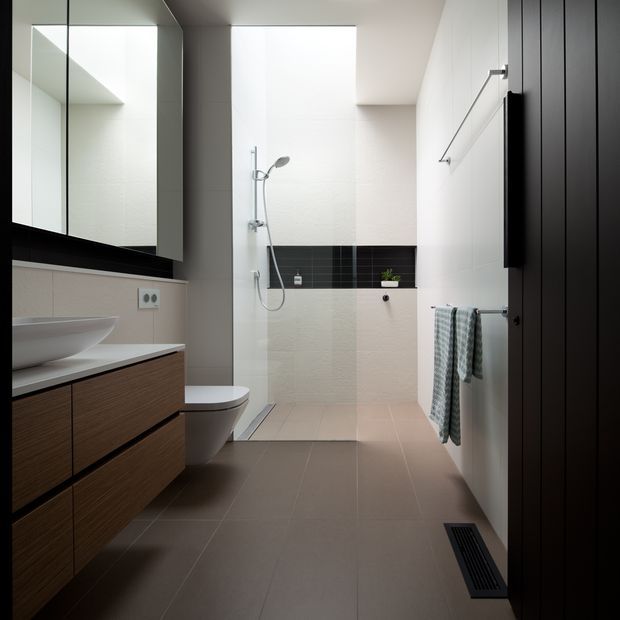 A contemporary bathroom with a walk-in shower, wall-mounted toilet, vessel sink, and floating dark timber vanity. Large mirrored cabinetry reflects the bright, compact space. The room uses pale textured wall tiles, dark horizontal feature tiles in the shower, warm grey floor tiles, white sanitaryware, and dark timber joinery.