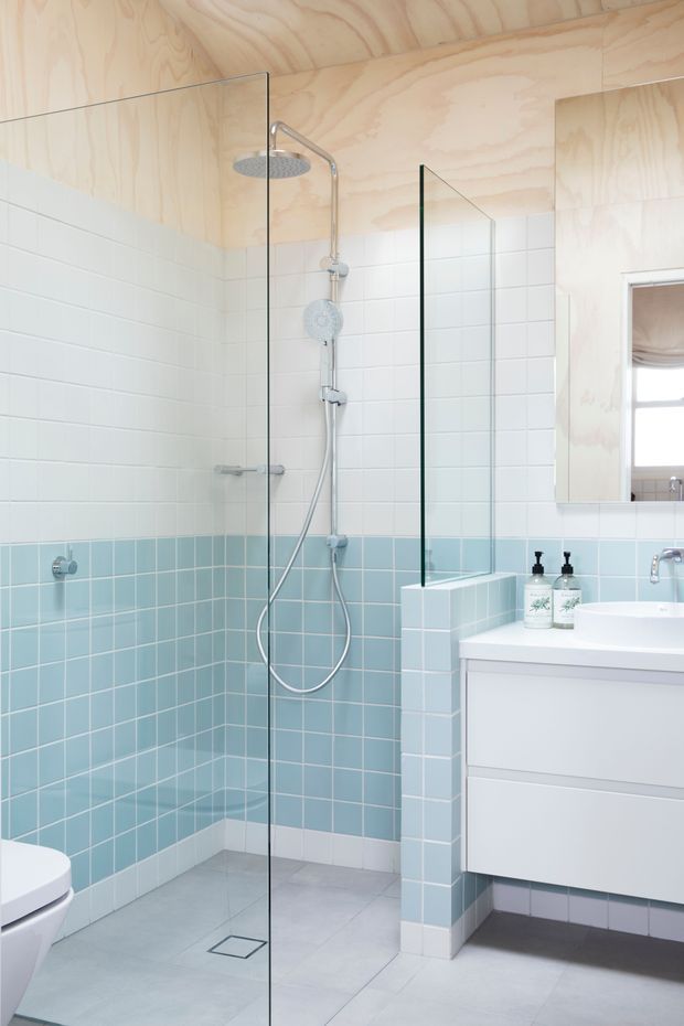 Bright contemporary bathroom featuring a walk-in shower enclosed by frameless glass, pale blue and white tiled walls, light grey floor tiles, a white floating vanity, and a natural plywood-lined ceiling and upper walls. Chrome shower and tapware, a partial toilet, and a mirrored cabinet are visible.