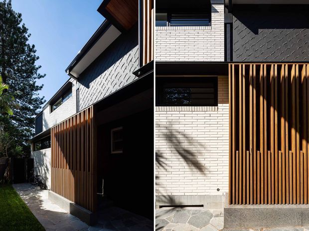 A contemporary multi-level residential facade viewed from outdoors, featuring white brick walls, dark textured wall panels, timber soffits, and a prominent vertical timber privacy screen. Deep roof overhangs, horizontal windows, strong shadow lines, and a paved side walkway create a layered modern exterior composition.